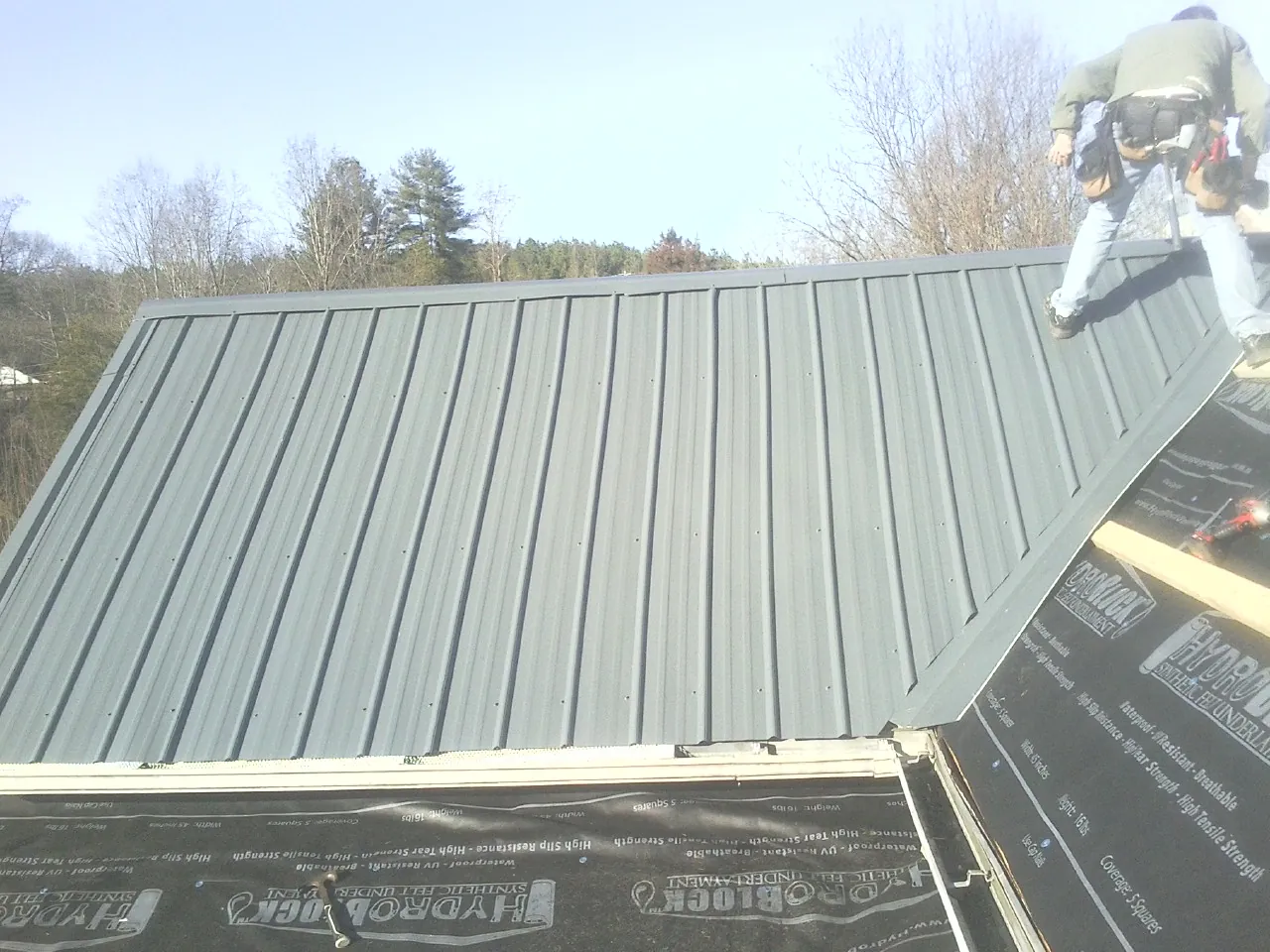 Crew installing dark green standing seam panels over synthetic underlayment in Northford