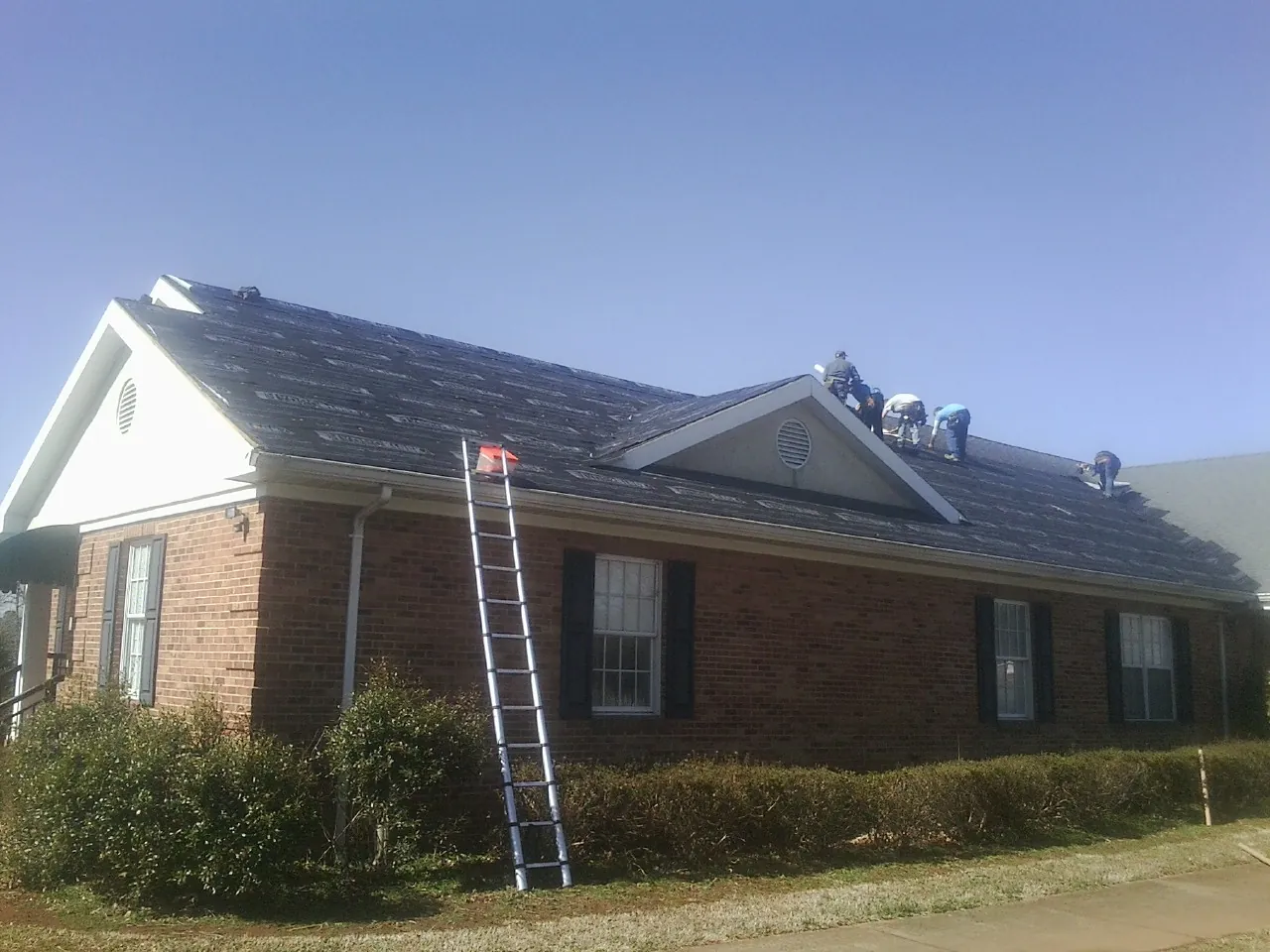 Crew tearing shingles off a brick ranch roof with a ladder set — Emergency Roof Repair work by our crew in Northford