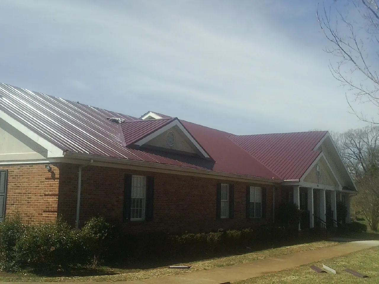 Red metal roof with gabled entries on a long brick building, from a Hail Damage Roof Repair job in Northford