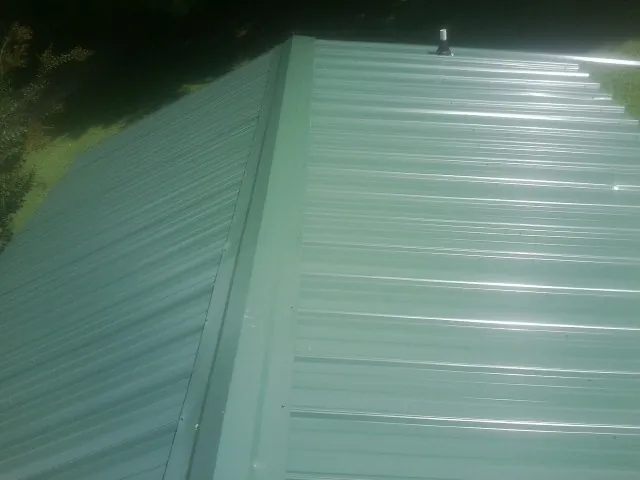 New green metal panels meeting at the ridge of a roof — Flat Roof Repair work by our crew in Northford