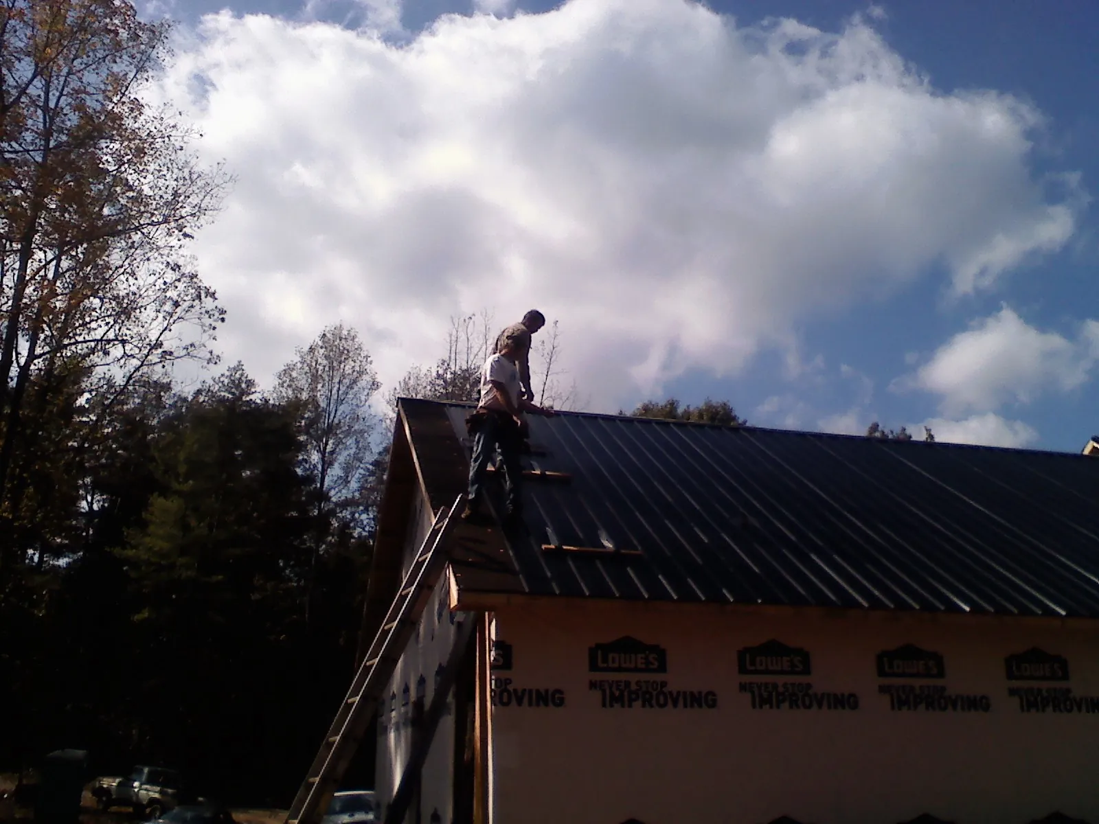 Roofer fastening dark metal panels high against a cloudy sky, from a Roof Inspection job in Northford