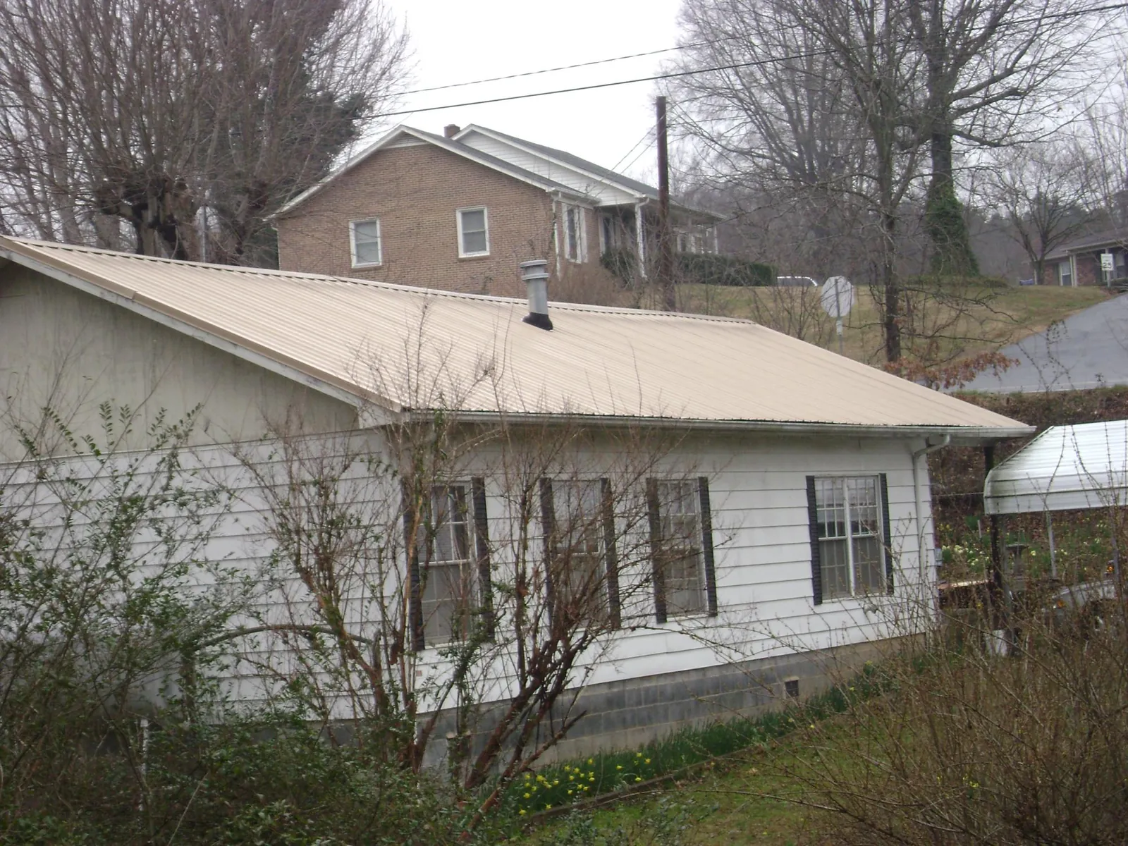 Tan metal roof on a white sided house set into a hillside — Commercial Roofing by Roofing Brothers in Northford