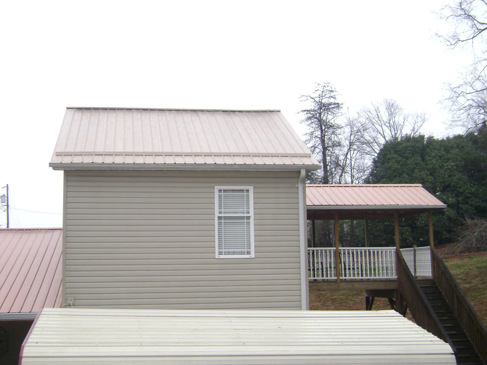 Tan metal roofs on a two story addition and attached porch, from a Roof Replacement job in Northford